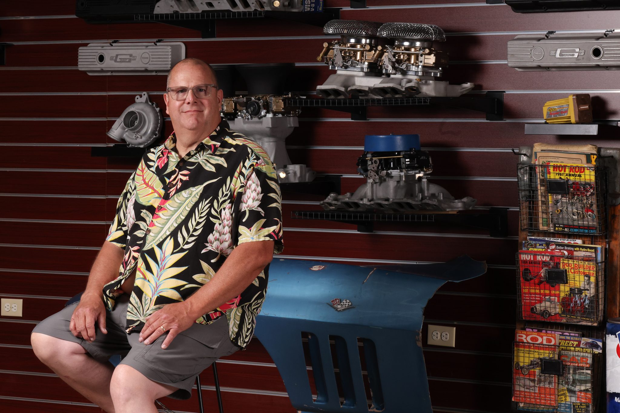 Environmental portrait of a collector seated against a wall of vintage carburetors and hot rod memorabilia — A2 Portraits, Ann Arbor