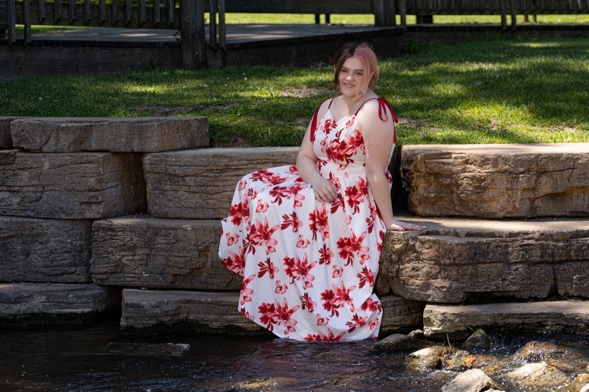 Senior portrait of Peyton seated on stone steps above a creek in a red floral dress — Ann Arbor fine art portraiture, A2 Portraits