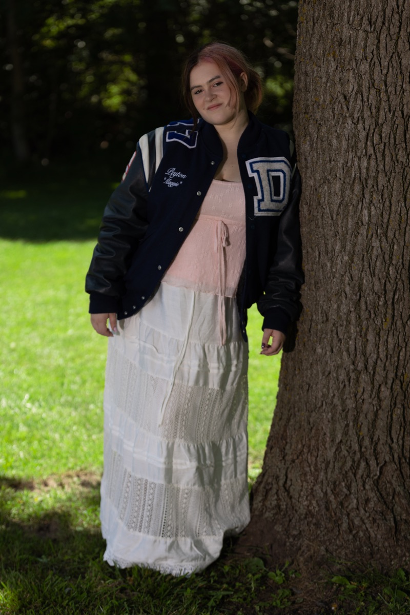 Senior portrait of Peyton in a letterman jacket leaning against a tree — A2 Portraits, Ann Arbor