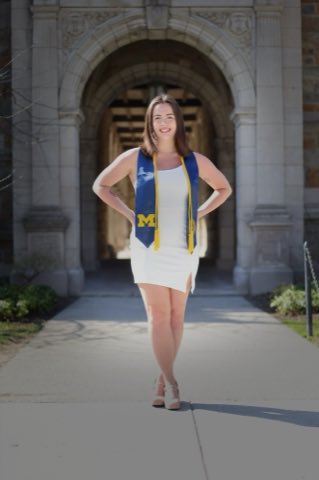 College graduation portrait of Sam in a white dress and M stole, standing on the walkway before a Gothic arch of the University of Michigan Law Quad